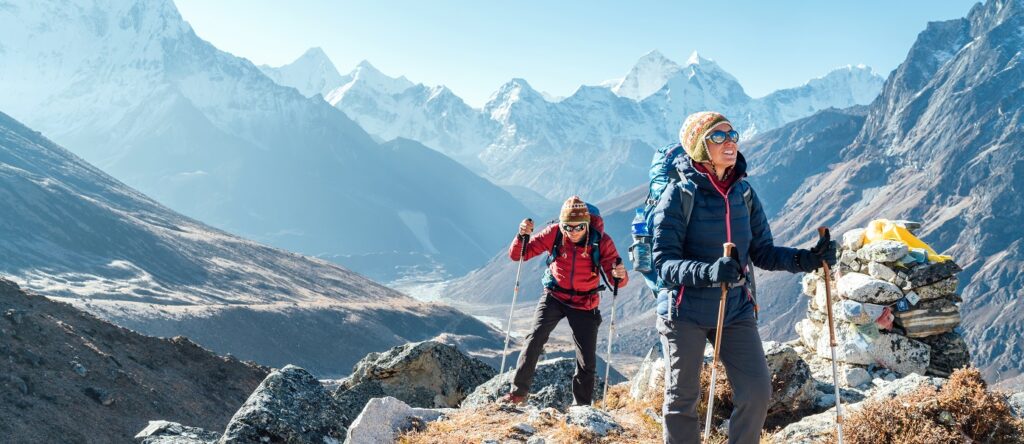 Para turystów - korzystających z ubezpieczenia turystycznego INTER Tour 365 - w drodze do bazy pod Everestem z plecakami i kijkami trekkingowymi, w tle szczyt Ama Dablam