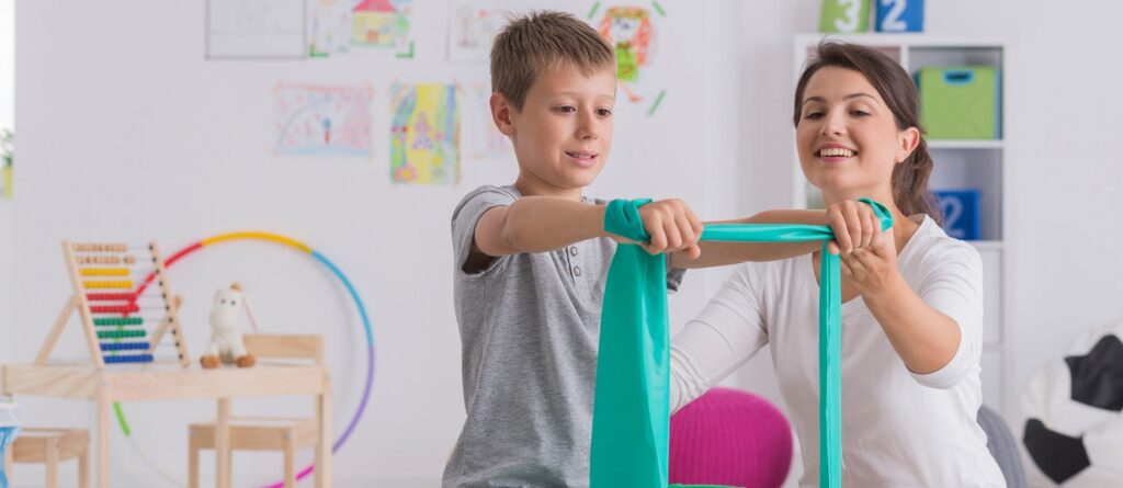 Fizjoterapeuta i chłopiec siedzący na piłce gimnastycznej - ćwiczenia rehabilitacyjne dla dzieci