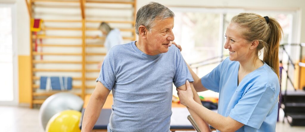 Fizjoterapeuta pomaga starszemu mężczyźnie w terapii ruchowej - rehabilitacja seniorów