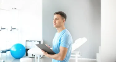 Fizjoterapeuta stoi w gabinecie i korzysta z ubezpieczenia zdrowotnego od INTER Polska.