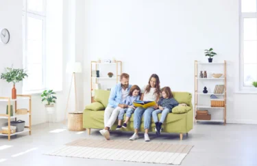 Medyk siedzi na kanapie z żoną i dziećmi, korzystając z oferty ubezpieczeń życia i profesjonalnej opieki medycznej INTER Polska.